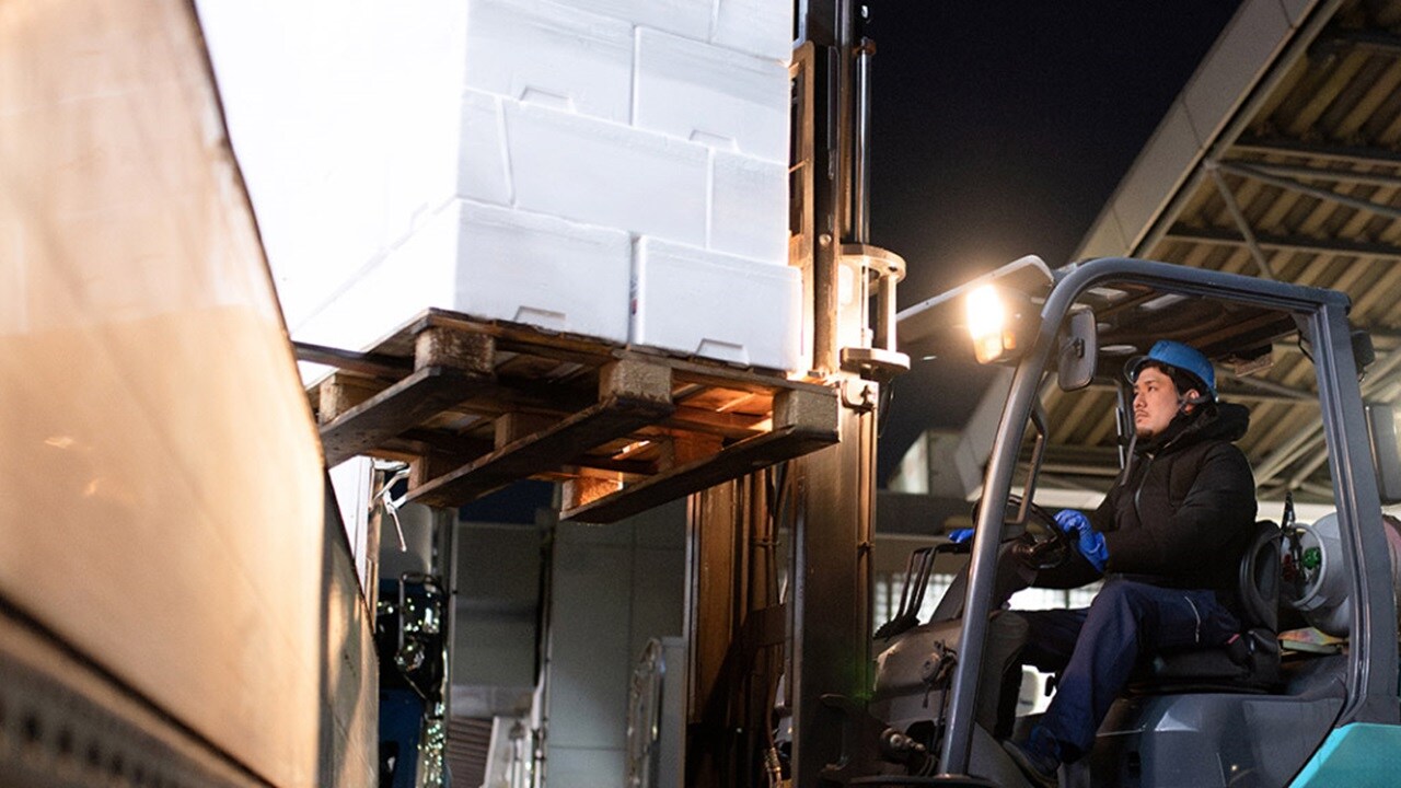 A man operates a forklift truck, lifting a pallet in a warehouse setting.
