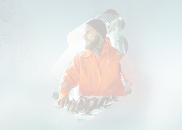 A man wearing an orange jacket stands beside a table, facing forward with a calm demeanor.