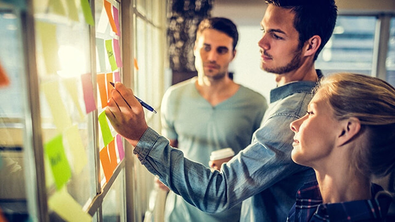 三位东升国际员工在办公室里，其中一人正在便签条上写字。