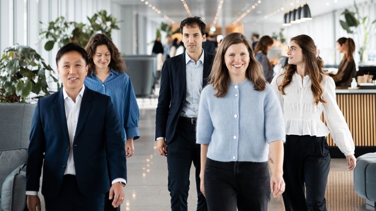 A diverse group of professionals walking together through a bright, modern office space, smiling and appearing engaged and confident.