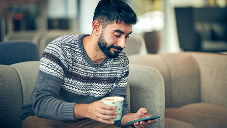 Person sitting on a couch with a coffee in hand and watching his smartphone