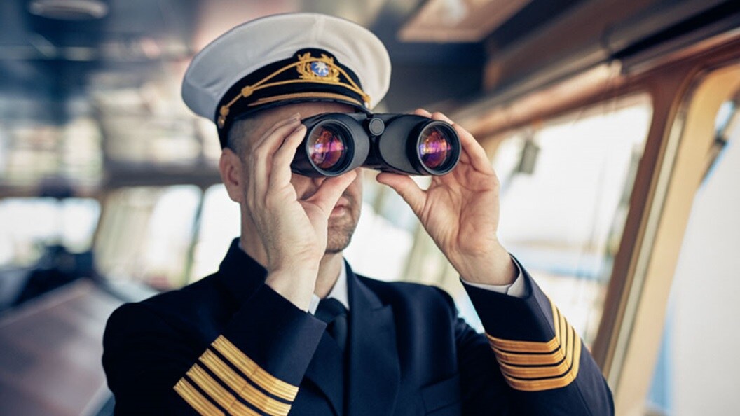 A ship captain looks through binoculars