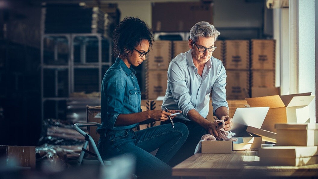 两个人站在办公桌旁，检查打开的装有鞋子的包装，这说明客户体验在物流中的重要性。
