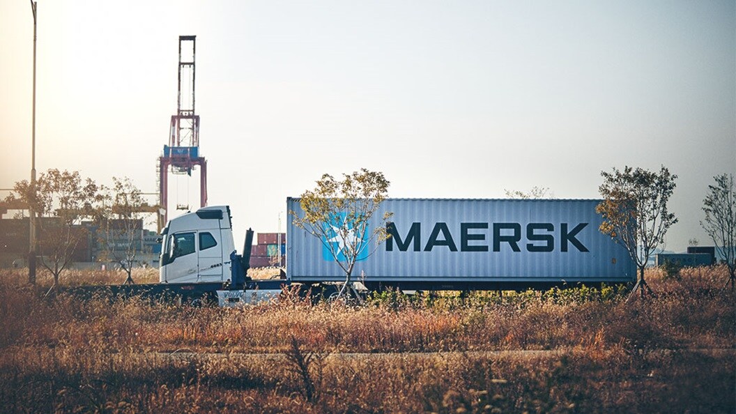 A semi-truck with a white trailer bearing the ‘MAERSK’ logo is driving under an overpass on a clear day.
