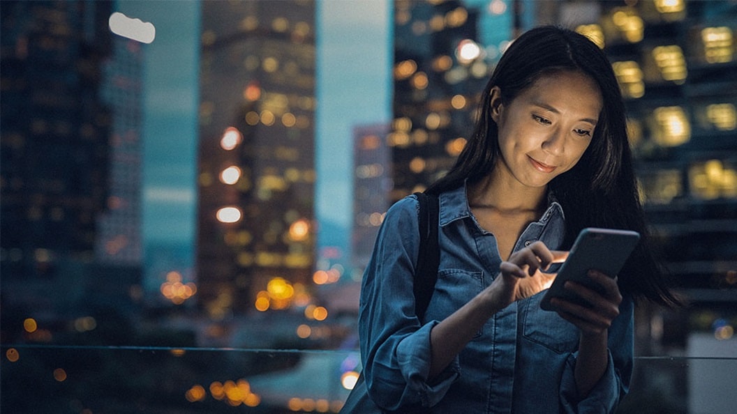 Woman using a smartphone at night with city lights in the background.