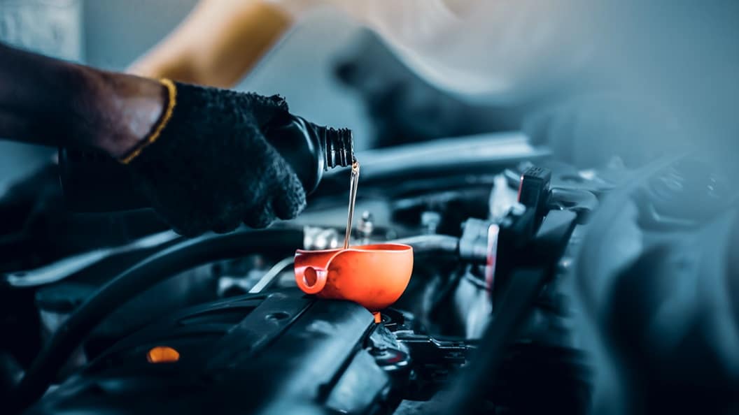 A close-up of a mechanic’s hand pouring engine oil into a car engine using an orange funnel.