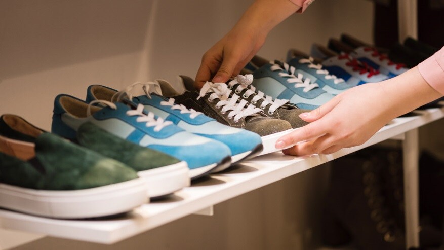 Person arranging a row of sneakers and casual shoes on a store shelf.