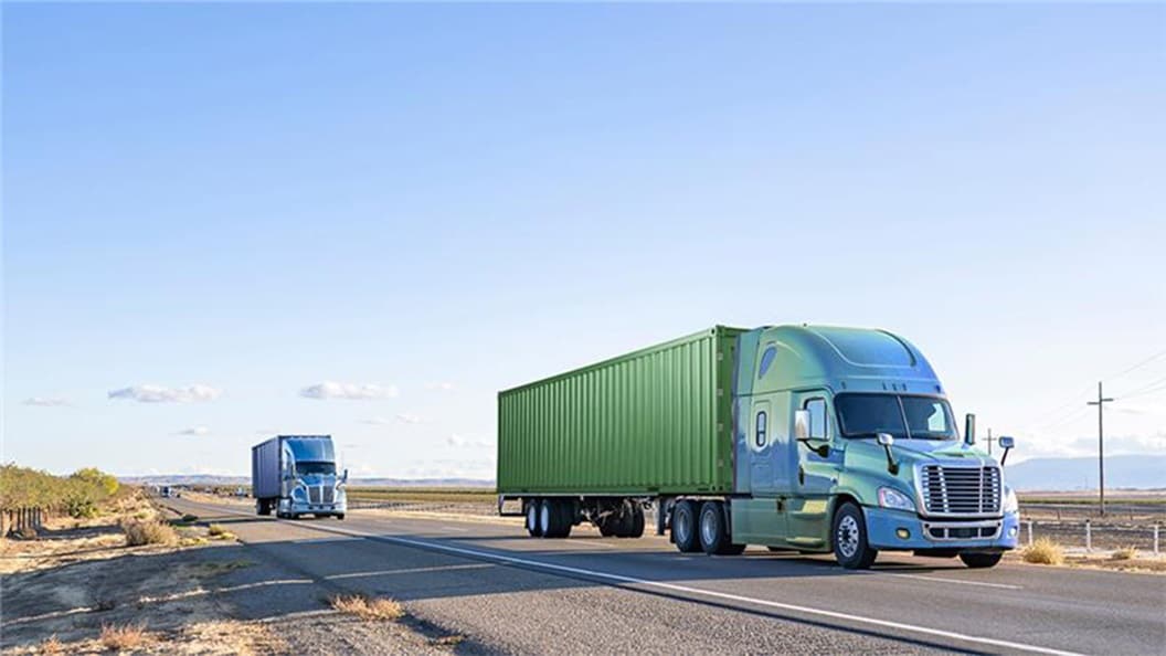 Two large trucks traveling down a highway.