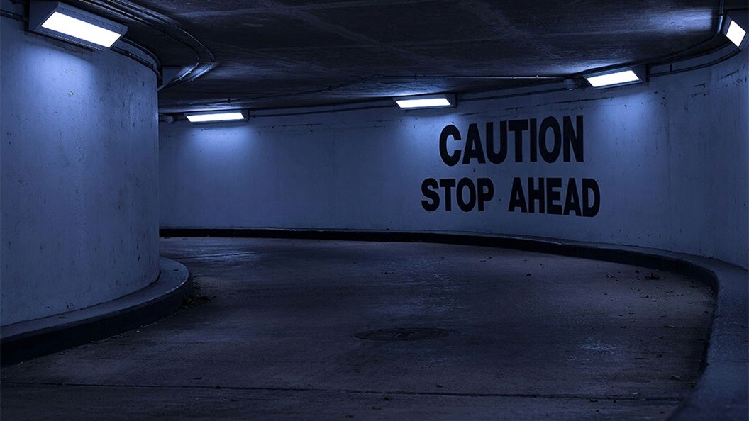 A sign on a parking garage ramp wall that says Caution Stop Ahead.