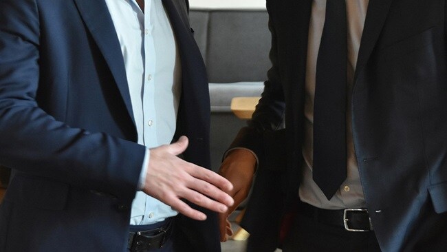 Two men in suits shaking hands in a professional setting, symbolizing agreement or partnership.