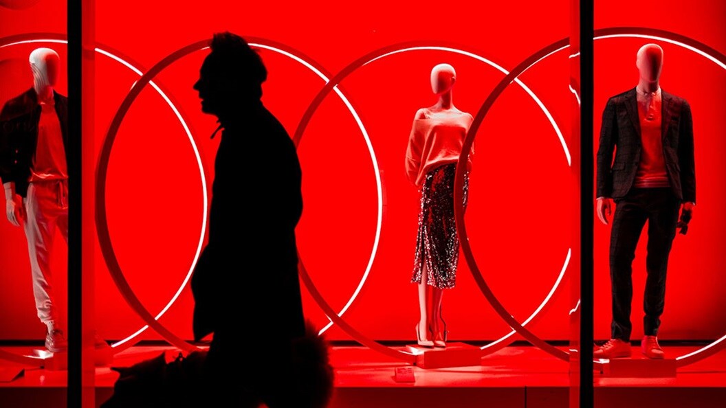 A man and dog walking in front of a trendy fashion clothing store lit with red light