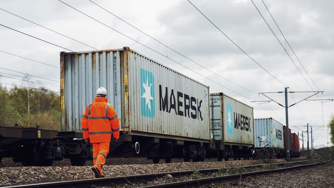 Rear view of a worker in protective gear walking towards Maersk containers carrying inland rail cargo.