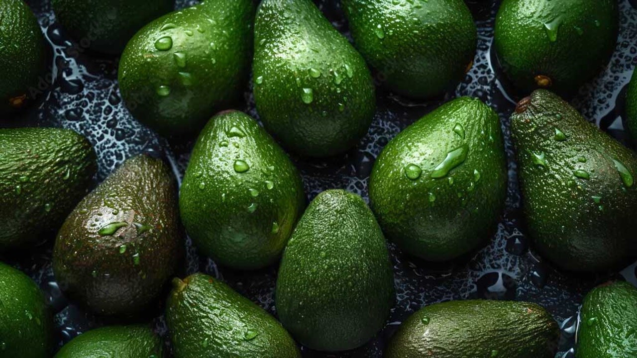 A pile of ripe avocados resting on a smooth black surface.