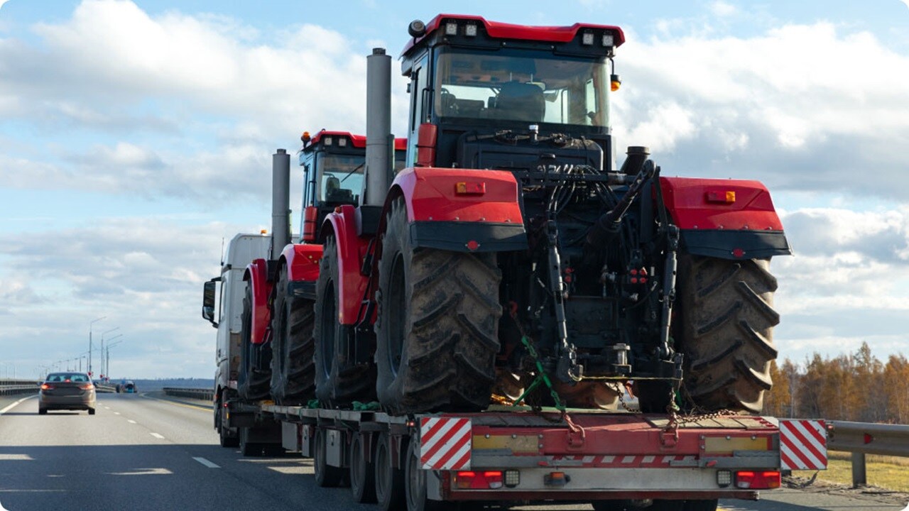 A tractor trailer with three large tires mounted on the back, parked on a gravel surface.