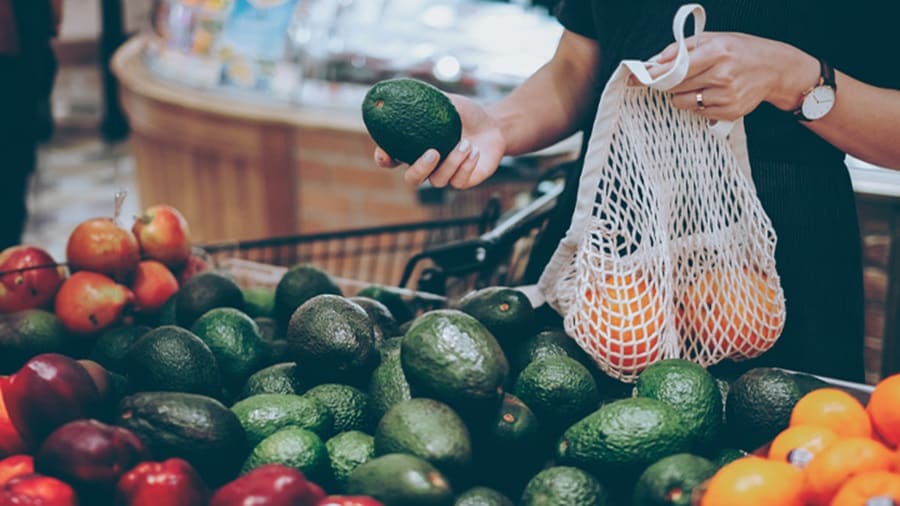 A set of hands choosing avocados in a supermarket