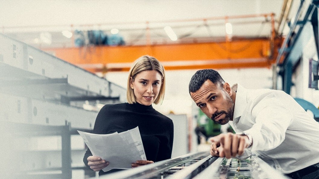 A woman holds papers while a man stands next to her, pointing his finger to demonstrate. 