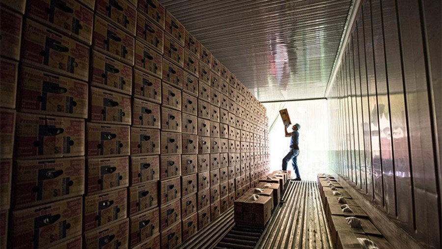 A worker stacks boxes inside a shipping container filled with cartons.