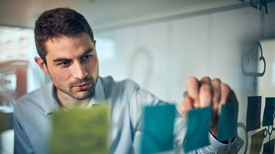 Man placing sticky notes on a glass wall.