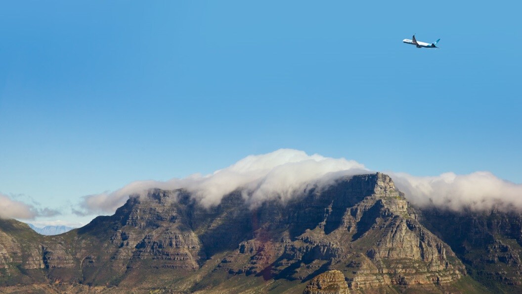 Airplane flying over mountains with clouds at the peaks.