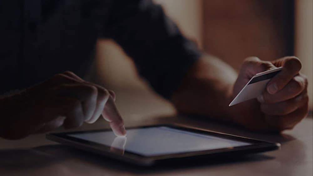 一位用信用卡在平板电脑上进行线上支付的人员的手部特写。